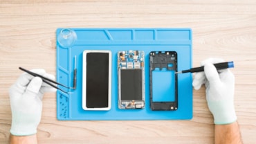 Top view of a technician holding some tools and preparing to repair an old broken smartphone. Young man looking at the inside hardware of a cellphone