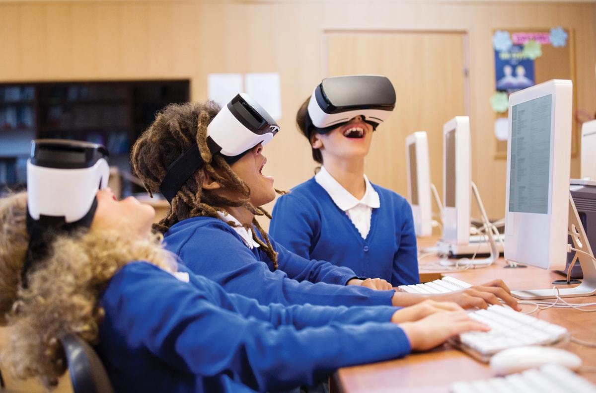 Mixed race group of excited students sitting in a computer lab at school and using virtual reality goggles.