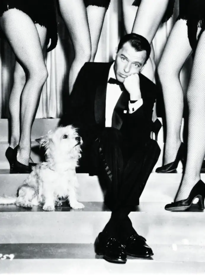 Frank Sinatra and a dog, sitting on some stairs with sexy legs surrounding him in a scene from the film 'Pal Joey', 1957. (Photo by Columbia Pictures/Getty Images)