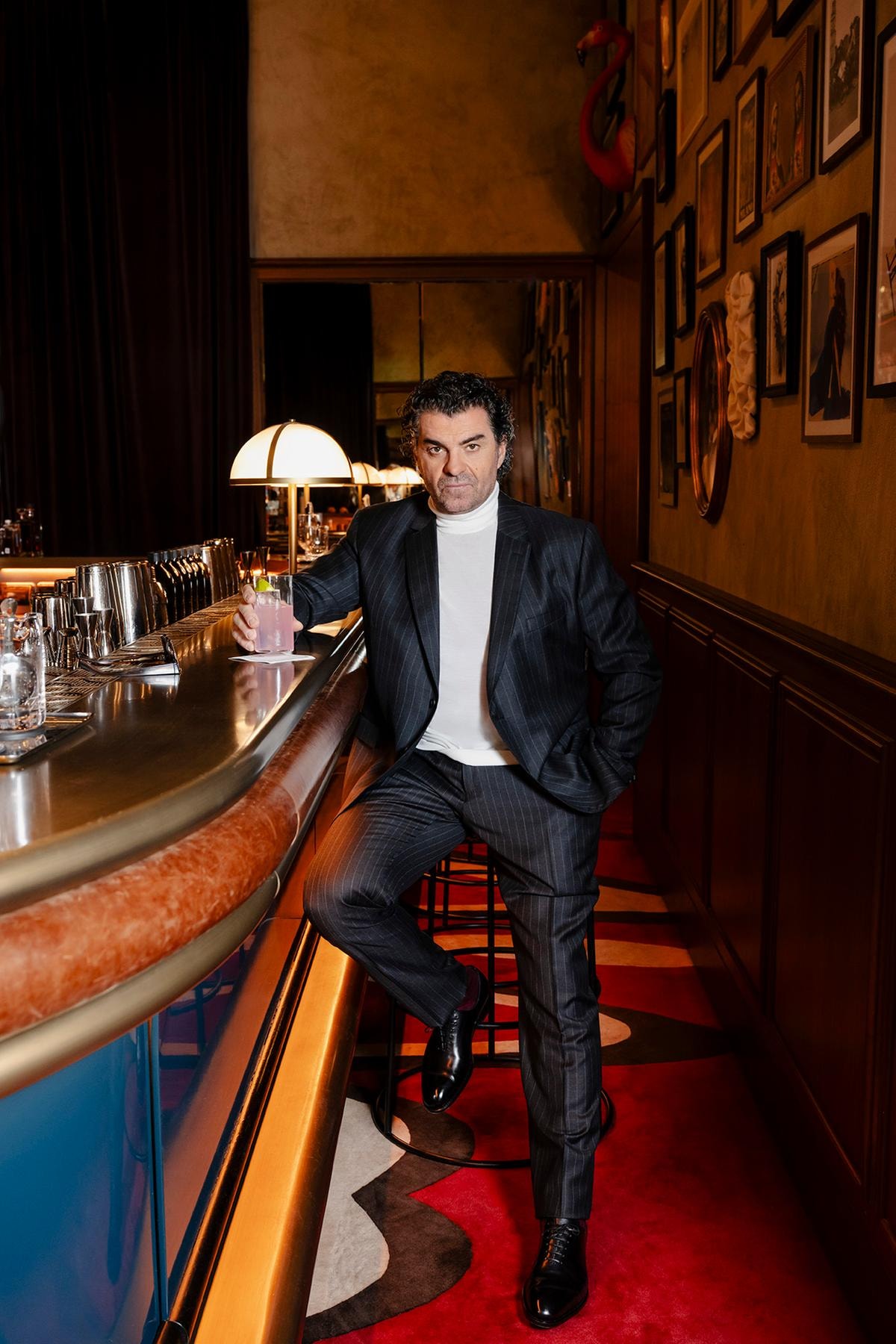 Alberto Tomba indossa un abito sartoriale in pura lana in tessuto gessato grigio, lupetto in lana e seta bianco, scarpe nere stringate con costruzione Tramezza in vitello semi lucido e occhiali da sole, tutto di Ferragamo.