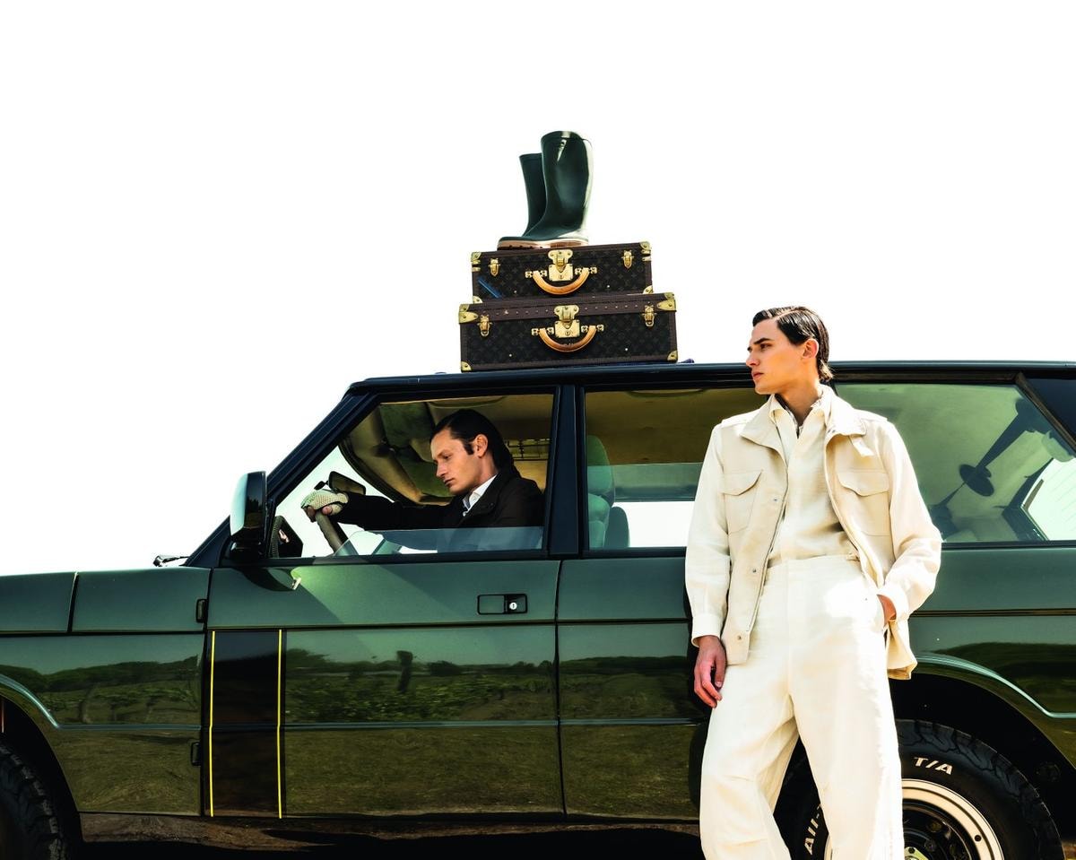 In primo piano, gilet con tasche applicate, camicia morbida, pantaloni e cache-col in lino, tutto di di Loro Piana. Seduto sulla Range Rover Classic by Vinile, sahariana in lino, camicia in cotone, pantalone in lino, tutto Kiton; guanti in pelle e cotone, Vinile per Restelli. Sopra, set di valigie in tela monogram con angoli e chiusura in ottone dorato, Louis Vuitton; stivali in gomma, Hunter.