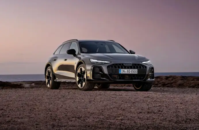 ¾ Front view of the Audi A6 allroad (plateau grey metallic) against a calm sea horizon at dusk.