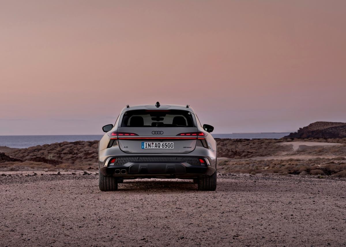 Rear view of the Audi A6 allroad (plateau grey metallic) with digital OLED rear lights 2.0 in a barren coastal landscape.