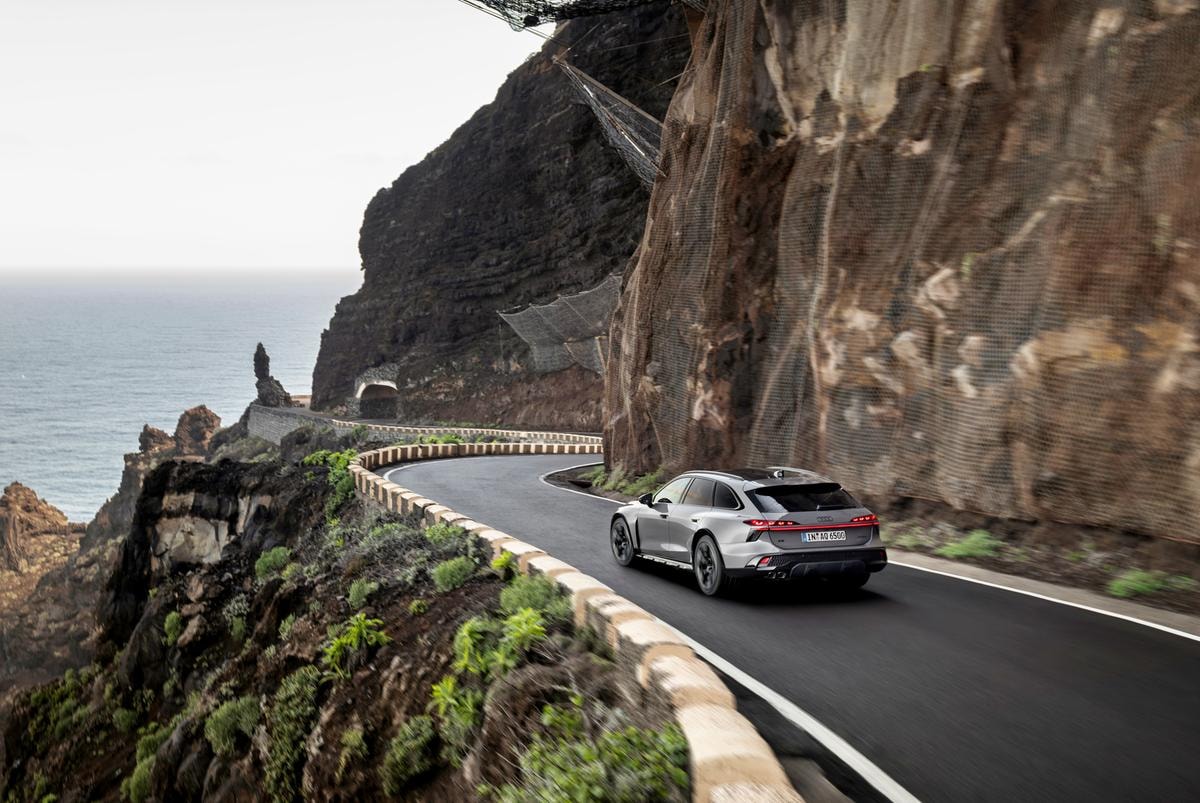Three-quarter rear view of Audi A6 allroad (plateau grey metallic) on a winding coastal road (dynamic shot).